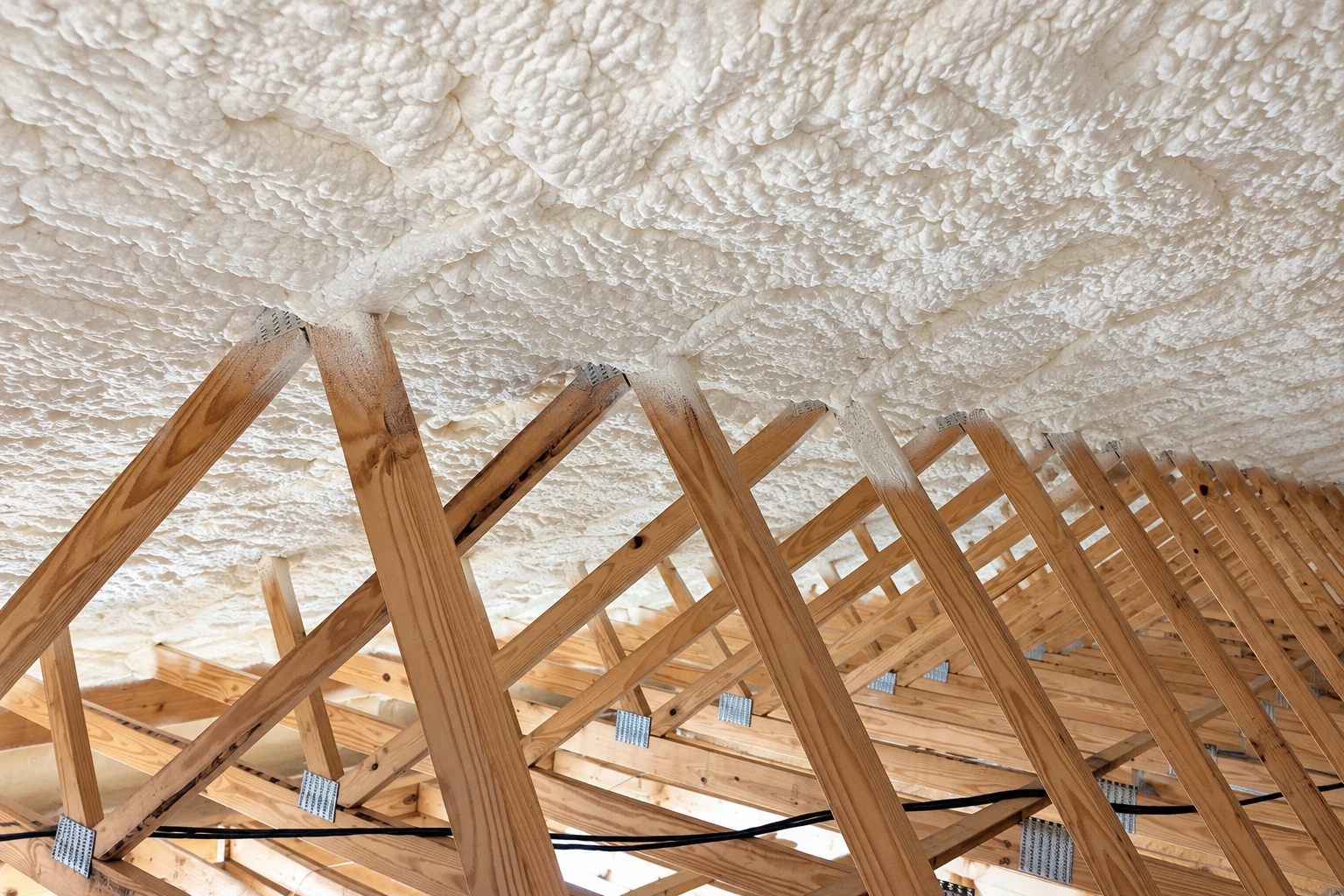 Exposed attic roof trusses are coated with thick white spray foam insulation.