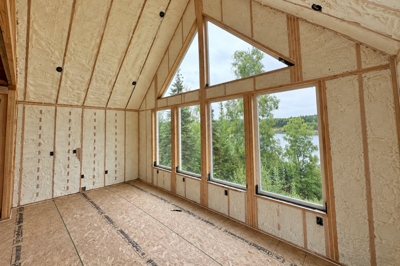 Closed-cell spray foam coats the walls and sloped ceiling of an unfinished room with large windows.