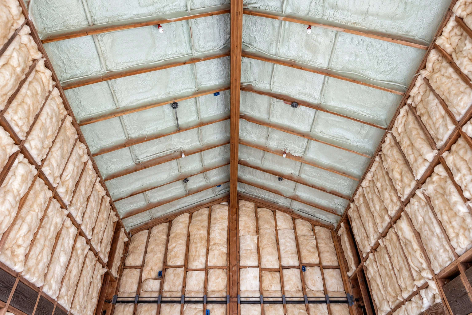 Foam insulation fills the roof panels and pale fiberglass batts line the walls of a wooden-framed attic.