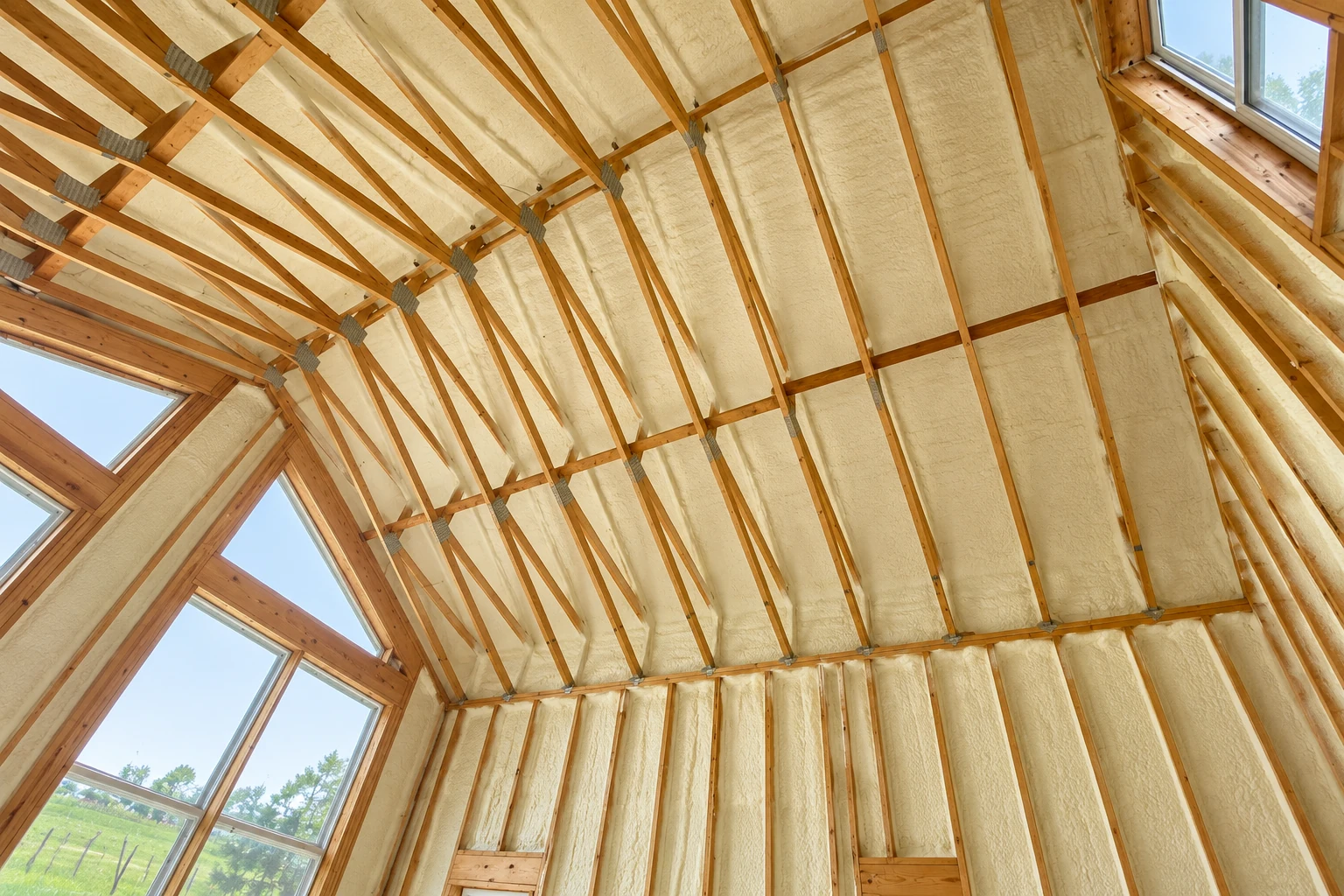 Cream-colored insulation fills the roof and walls of a timber-framed home beneath large windows.